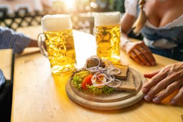 Traditional Bavarian Obatzda with pretzels and radishes and beer mugs, man and young woman in tracht in the background at beer garden or oktoberfest, Munich, Germany- Stock Photo or Stock Video of rcfotostock | RC Photo Stock