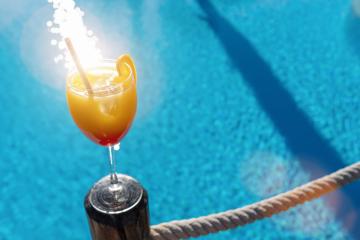 Tropical cocktail, garnished with a orange slice, set against a sparkling blue pool at caribbean island hotel - Stock Photo or Stock Video of rcfotostock | RC Photo Stock