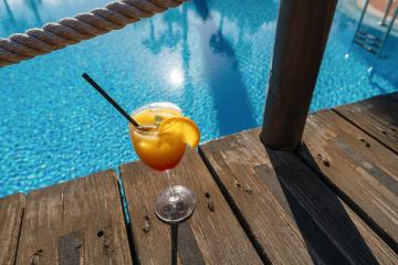 Tropical cocktail on a wooden deck by a pool, featuring a blue water background and rope railing at caribbean island hotel - Stock Photo or Stock Video of rcfotostock | RC Photo Stock