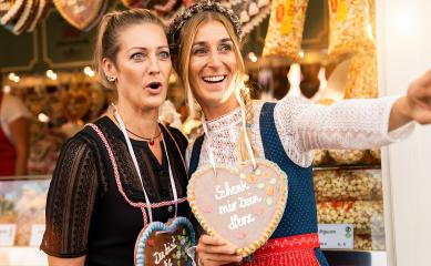 Two astonished girlfriends together on a Bavarian fair or oktoberfest or duld in national costume or Dirndl with Schenk mir dein Herz (German: Give me your heart) written on gingerbreads heart- Stock Photo or Stock Video of rcfotostock | RC Photo Stock
