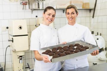 Two bakers smiling and holding a tray of chocolate-covered gingerbreads in a bakery, proudly presenting their freshly made treats in a professional baking environment : Stock Photo or Stock Video Download rcfotostock photos, images and assets rcfotostock | RC Photo Stock.: