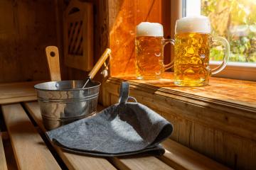 Two beer mugs with frothy beer rest on a ledge, catching sunlight. Nearby, a metal bucket, a ladle, and finnish Sauna hats on a wooden bench.  spa and wellness concept image : Stock Photo or Stock Video Download rcfotostock photos, images and assets rcfotostock | RC Photo Stock.: