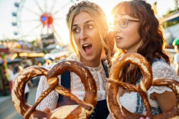 Two girlfriends look amazed with pretzel or brezen on a Bavarian fair or oktoberfest or duld in national costume or Dirndl : Stock Photo or Stock Video Download rcfotostock photos, images and assets rcfotostock | RC Photo Stock.: