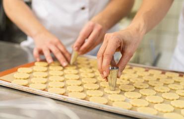 Two people are preparing cookies by cutting out the center of dough shapes on a baking tray using metal cutters. The dough is arranged neatly on a silicone baking mat. : Stock Photo or Stock Video Download rcfotostock photos, images and assets rcfotostock | RC Photo Stock.: