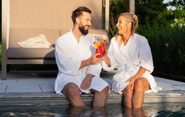 Two people in white bathrobes laughing and toasting with red drinks by a pool at sunset at a spa hotel- Stock Photo or Stock Video of rcfotostock | RC Photo Stock