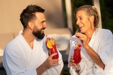 Two people in white robes laughing and drinking cocktails in the sunlight at a wellness hotel- Stock Photo or Stock Video of rcfotostock | RC Photo Stock