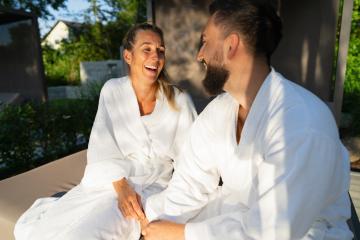 Two people in white robes sitting on a couple's lounger outdoors and having fun laughing together at a hotel- Stock Photo or Stock Video of rcfotostock | RC Photo Stock