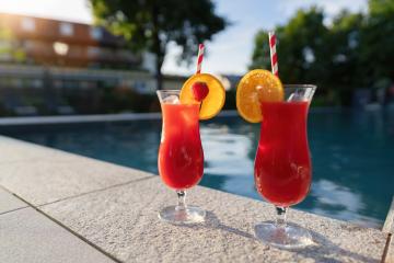 Two red cocktails with fruit garnishes by a poolside, reflecting the warm sunset light- Stock Photo or Stock Video of rcfotostock | RC Photo Stock