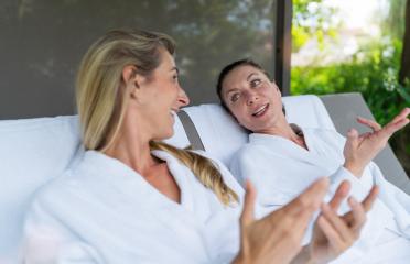 Two women in white bathrobes talking and gesturing on outdoor loungers at a spa wellness resort- Stock Photo or Stock Video of rcfotostock | RC Photo Stock