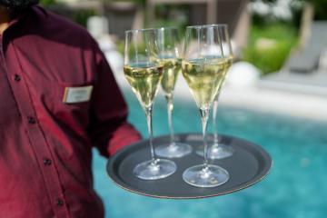 Waiter in a red shirt holding a tray with three glasses of champagne by a pool. Hotel travel concept image- Stock Photo or Stock Video of rcfotostock | RC Photo Stock