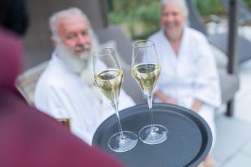 Waiter offering champagne to a smiling senior couple in white bathrobes at a hotel- Stock Photo or Stock Video of rcfotostock | RC Photo Stock