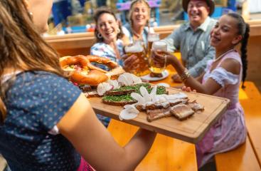 Waitress serving a wooden platter of traditional German food to a group of joyful people in a beer tent at oktoberfest festival or dult in germany- Stock Photo or Stock Video of rcfotostock | RC Photo Stock