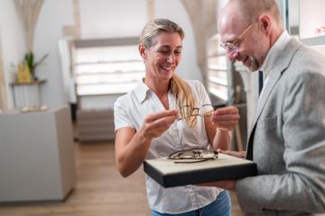 Woman happily trying on glasses with optician presenting eyewear options. Optical store interior in the background.- Stock Photo or Stock Video of rcfotostock | RC Photo Stock