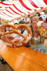 woman holding a large pretzel and drinking a mug of beer at Oktoberfest, with colorful striped tents overhead and friends in the background in munich : Stock Photo or Stock Video Download rcfotostock photos, images and assets rcfotostock | RC Photo Stock.: