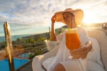 Woman in a sun hat enjoying a cocktail at tropical beach hotel on a sunny terrace with a pool in the background- Stock Photo or Stock Video of rcfotostock | RC Photo Stock