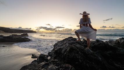 Woman in a white dress and straw hat standing on rocks at the beach during a vibrant sunset- Stock Photo or Stock Video of rcfotostock | RC Photo Stock