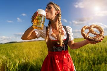 Woman in Bavarian dress drinking beer and holding a pretzel in a sunny wheat field at Oktoberfest in munich- Stock Photo or Stock Video of rcfotostock | RC Photo Stock