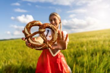 Woman in Bavarian tracht playfully holding a pretzel in a field, with focus on the pretzel ready for Oktoberfest or dult festival in munich. : Stock Photo or Stock Video Download rcfotostock photos, images and assets rcfotostock | RC Photo Stock.: