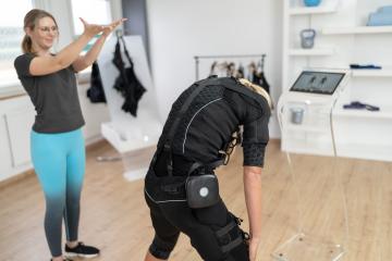 Woman in EMS suit performing exercises with trainer guidance and computer in a EMS - Studio- Stock Photo or Stock Video of rcfotostock | RC Photo Stock