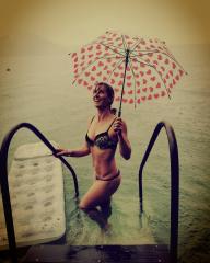 Woman in leopard print bikini standing in water, holding a pink heart-patterned umbrella, smiling, overcast day, near ladder and inflatable mat, enjoying the rain, scenic lake backdrop
 : Stock Photo or Stock Video Download rcfotostock photos, images and assets rcfotostock | RC Photo Stock.: