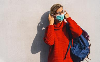 woman in round glasses takes off her turquoise face mask from her nose, dressed in a vibrant red sweater, with a distinct shadow behind her on a concrete wall : Stock Photo or Stock Video Download rcfotostock photos, images and assets rcfotostock | RC Photo Stock.: