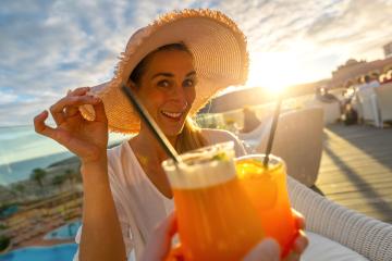 Woman in sun hat smiling and toasting with a cocktail at tropical beach hotel on sunset with blurry background- Stock Photo or Stock Video of rcfotostock | RC Photo Stock