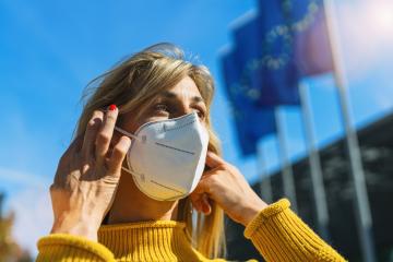 Woman in the city puts on a medical anti virus protection knN95 FFP2 face mask to prevent others from corona virus COVID-19 and SARS cov 2 infection with european flags  in the background : Stock Photo or Stock Video Download rcfotostock photos, images and assets rcfotostock | RC-Photo-Stock.: