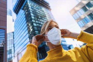Woman in the city puts on a medical anti virus protection knN95 FFP2 face mask to prevent others from corona virus COVID-19 and SARS cov 2 infection with skyscraper in the background : Stock Photo or Stock Video Download rcfotostock photos, images and assets rcfotostock | RC Photo Stock.:
