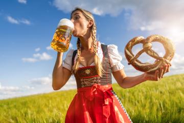 Woman in traditional Bavarian tracht enjoying a beer and pretzel in a sunny wheat field celebrating Oktoberfest festival in munich.- Stock Photo or Stock Video of rcfotostock | RC Photo Stock