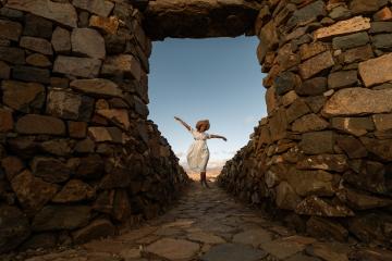 Woman in white dress and straw hat jumping joyfully in a stone archway at fuerteventura - Stock Photo or Stock Video of rcfotostock | RC Photo Stock