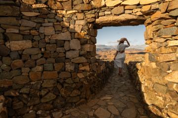 Woman in white dress and straw hat looking out from a stone archway at a mountainous landscape at fuerteventura - Stock Photo or Stock Video of rcfotostock | RC Photo Stock