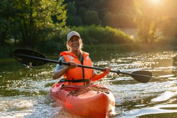 Woman joyfully paddling a red kayak in a river during sunset, surrounded by lush greenery. Kayak Water Sports concept image- Stock Photo or Stock Video of rcfotostock | RC Photo Stock