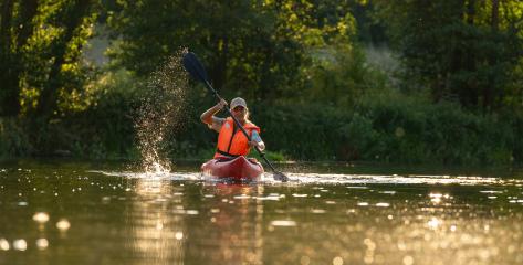 Woman kayaking in calm river waters at sunset, creating a splash with his paddle wearing an orange life jacket at summer. Kayak Water Sports concept image- Stock Photo or Stock Video of rcfotostock | RC Photo Stock