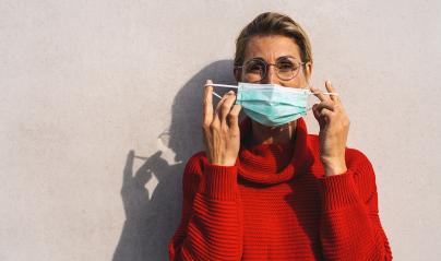 woman looks to camera in round glasses takes off her turquoise face mask from her nose, dressed in a vibrant red sweater, with a distinct shadow behind her on a concrete wall : Stock Photo or Stock Video Download rcfotostock photos, images and assets rcfotostock | RC Photo Stock.:
