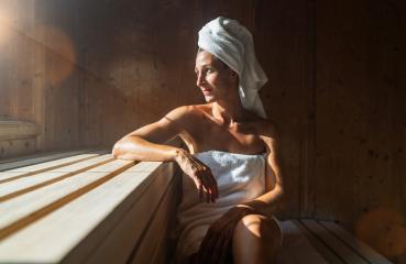 Woman sitting in a finnish sauna, leaning on one arm, with a towel wrapped around her head, sunlight streaming in at wellness spa hotel- Stock Photo or Stock Video of rcfotostock | RC Photo Stock