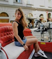 Woman sitting in a red horse-drawn carriage, wearing a black tank top, denim skirt, and sneakers, with long blonde hair, in a city street with buildings and a horse in the background, smiling
 : Stock Photo or Stock Video Download rcfotostock photos, images and assets rcfotostock | RC Photo Stock.: