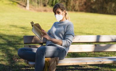 Woman sitting on bench in park and read a book with protection mask to prevent others from corona COVID-19 and SARS cov 2 infection. social distancing concept image- Stock Photo or Stock Video of rcfotostock | RC-Photo-Stock