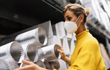 woman wearing a face mask and a yellow sweater examines silver ventilation ducts in a warehouse or store setting.  Corona safety Concept image : Stock Photo or Stock Video Download rcfotostock photos, images and assets rcfotostock | RC Photo Stock.: