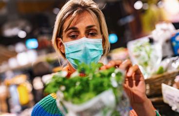 woman wearing a light blue face mask examines fresh basil in a bustling grocery store or supermarket, surrounded by an array of produce. Corona safety Concept image- Stock Photo or Stock Video of rcfotostock | RC Photo Stock