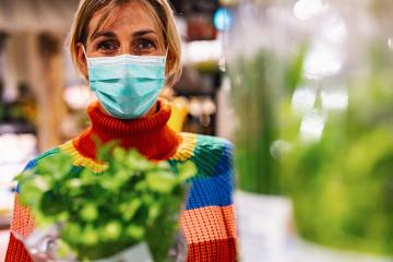 woman wearing a light blue face mask examines fresh basil in a bustling grocery store or supermarket, surrounded by an array of produce. Corona safety Concept image : Stock Photo or Stock Video Download rcfotostock photos, images and assets rcfotostock | RC Photo Stock.: