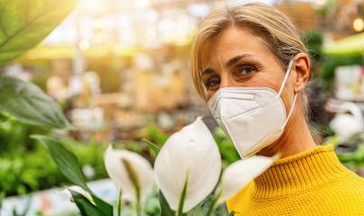 woman wearing a white face mask stands amidst lush greenery, appreciating a white flower, with a softly lit store backdrop. Shopping in a greenhouse or garden center concept image : Stock Photo or Stock Video Download rcfotostock photos, images and assets rcfotostock | RC Photo Stock.: