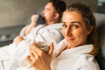Woman with a cup of tea smiling at camera, man in spa robe drinking tea in background at wellness resort- Stock Photo or Stock Video of rcfotostock | RC Photo Stock