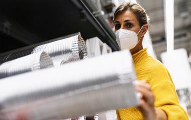woman with face mask and a yellow sweater examines silver ventilation ducts in a warehouse or store setting. Corona safety Concept image- Stock Photo or Stock Video of rcfotostock | RC Photo Stock