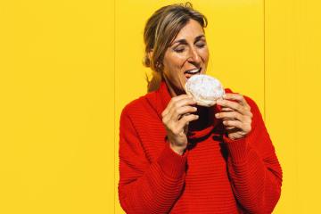 Woman with red sweater bite into a strawberry jam filled berliner doughnut against yellow wall : Stock Photo or Stock Video Download rcfotostock photos, images and assets rcfotostock | RC Photo Stock.: