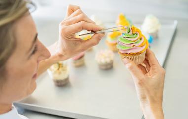women in pastry bakery as confectioner draped candy pearl topping on a colorful muffin  with tweezers : Stock Photo or Stock Video Download rcfotostock photos, images and assets rcfotostock | RC Photo Stock.: