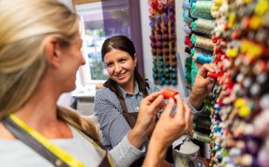 Work colleagues in a tailor shop, one in focus, share a moment in a sewing workspace. They're surrounded by colorful threads, with one holding a spool of red thread : Stock Photo or Stock Video Download rcfotostock photos, images and assets rcfotostock | RC Photo Stock.: