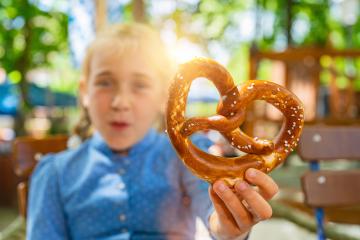 Youn girl holding Traditional Bavaria pretzel in Tracht, Dirndl having fun in Beer garden or oktoberfest in Bavaria, Germany- Stock Photo or Stock Video of rcfotostock | RC Photo Stock