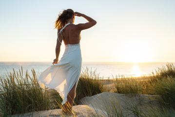 young attractive woman standin in dunes by sea beach looking to ocean at sunset- Stock Photo or Stock Video of rcfotostock | RC Photo Stock