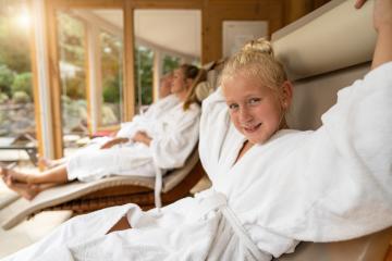 young girl smiling in the foreground, with her family relaxing in robes in the background, in a bright spa hotel lounge- Stock Photo or Stock Video of rcfotostock | RC Photo Stock