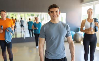 Young man in grey t-shirt smiling in a gym with other people in the background. Teamwork Concept image- Stock Photo or Stock Video of rcfotostock | RC Photo Stock